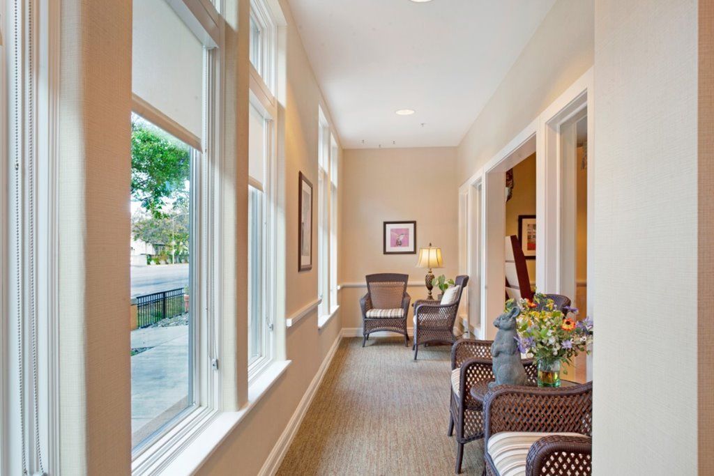 A bright hallway with large windows, adorned with comfortable seating and floral decor.
