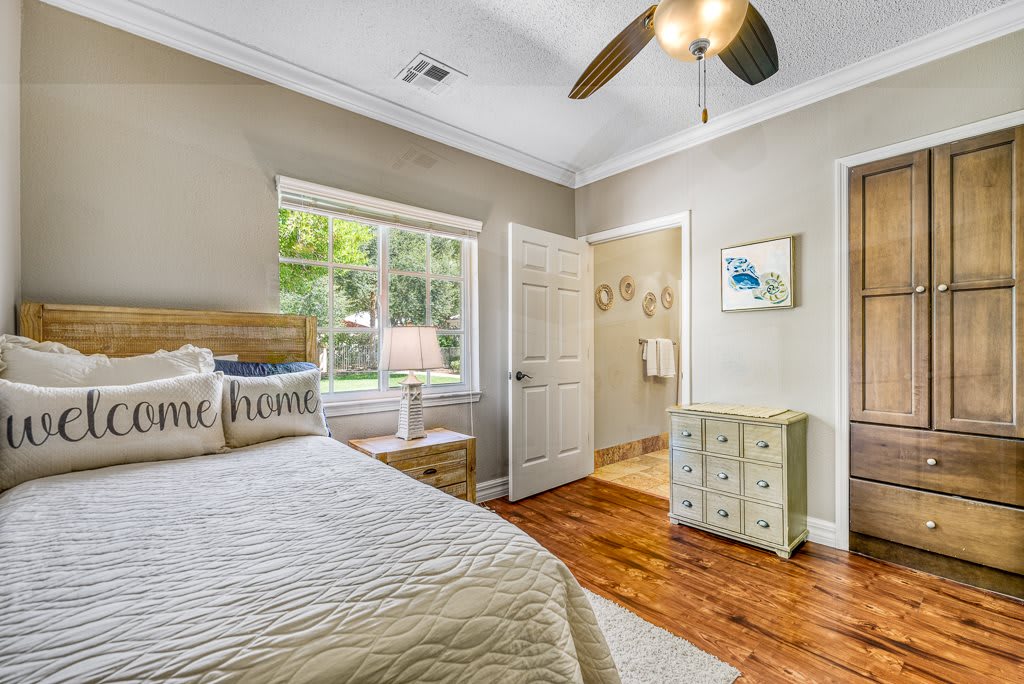 A cozy bedroom with a wooden floor, featuring a bed and dresser next to a window.