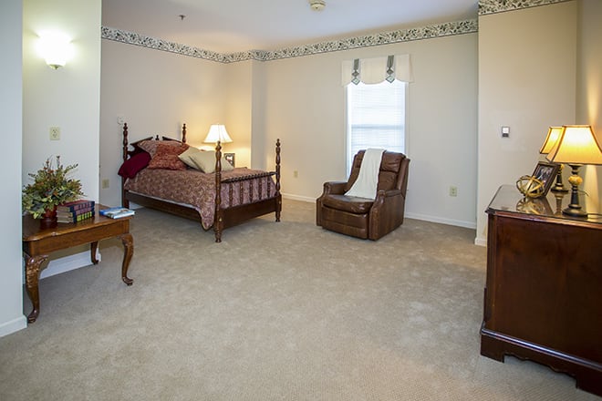 A cozy bedroom with a traditional wooden bed, armchair, and carpeted floor.