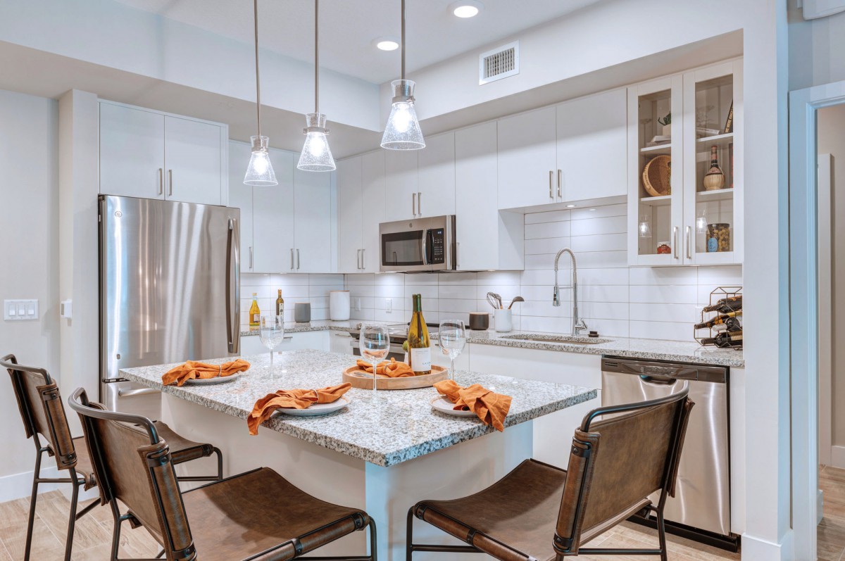 A modern kitchen with a sleek design featuring an island, pendant lighting, and stainless steel appliances.
