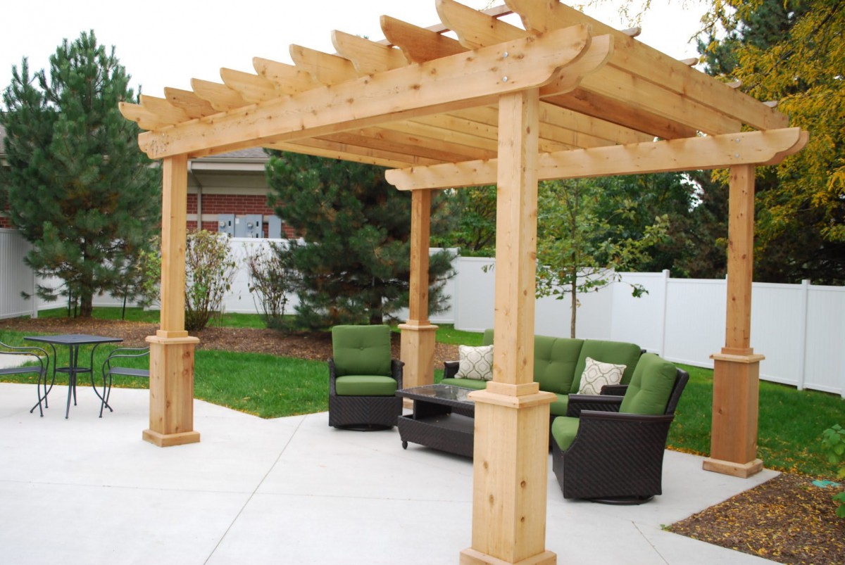 A wooden pergola with comfortable outdoor seating on a patio in a garden setting.
