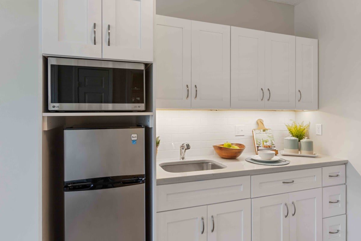 A modern kitchen with white cabinets, a small fridge, microwave, and a countertop with a sink.