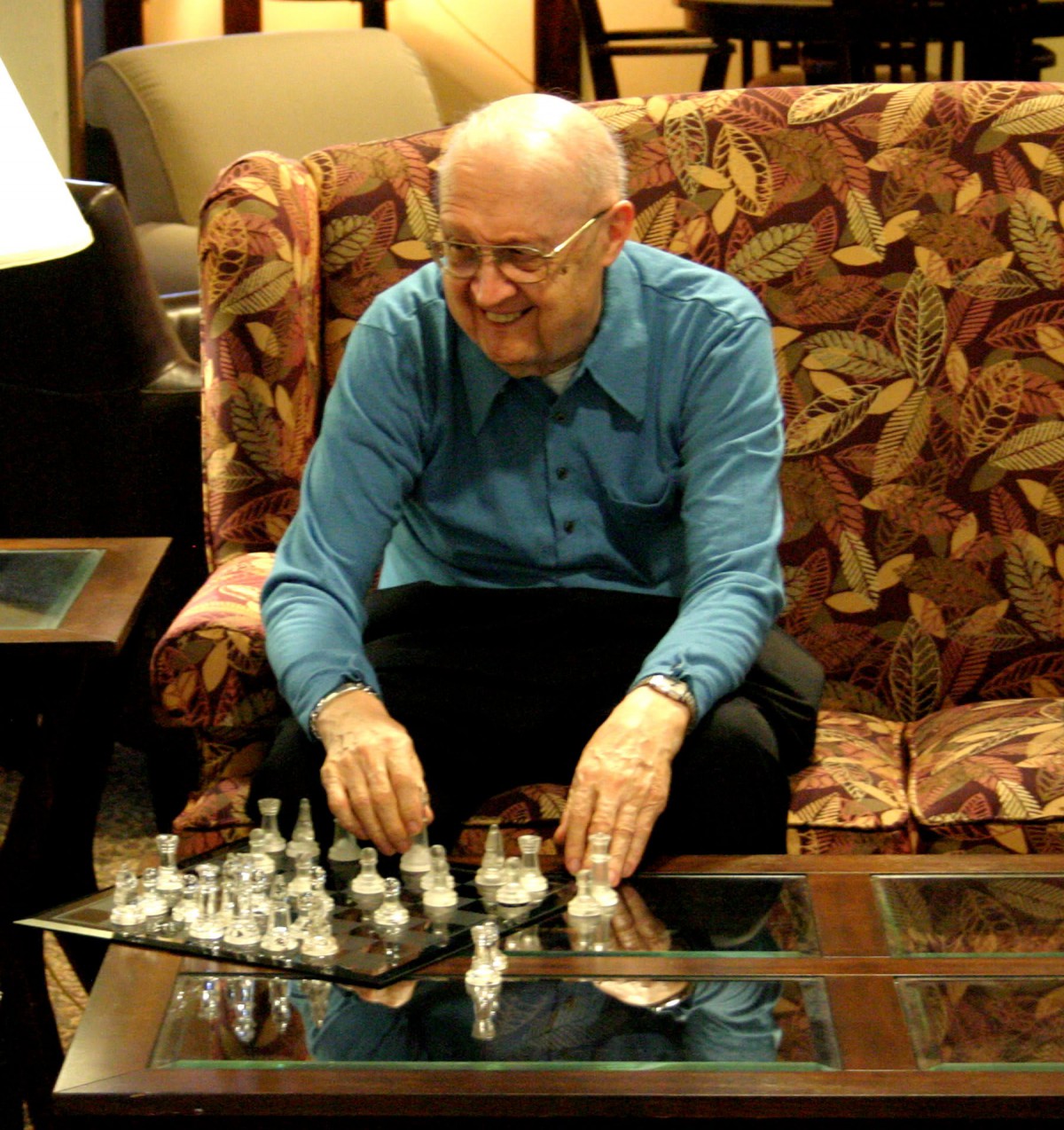 A man sitting on a couch setting up a chessboard on a glass table.