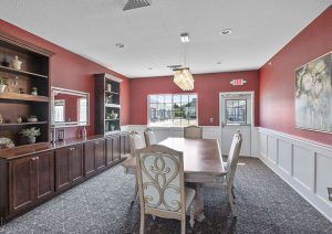 A stylish dining room with red walls, featuring a large table and upholstered chairs under a modern chandelier.