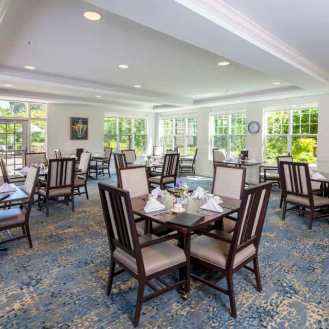 A well-lit dining room with several tables and chairs arranged neatly on a carpeted floor.