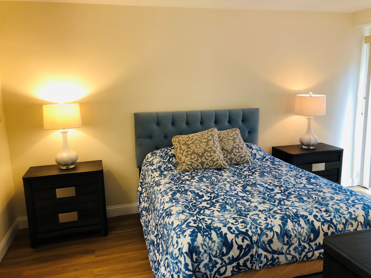 A cozy bedroom with a blue-patterned bedspread and matching nightstands with lamps.