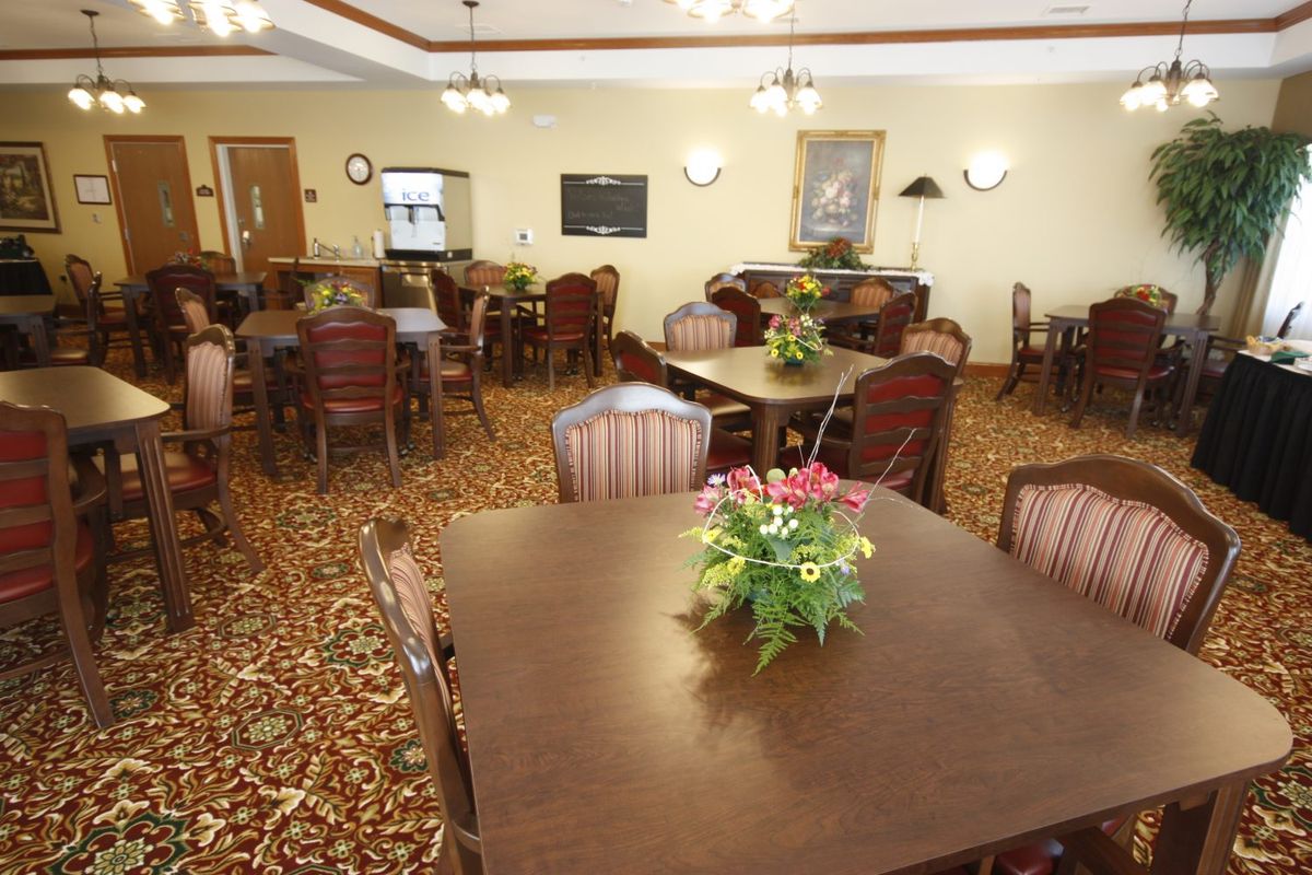 A cozy dining area with multiple tables and chairs, decorated with flowers and lit by warm overhead lighting.