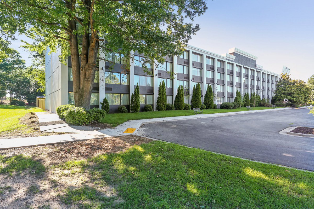 A modern office building surrounded by trees and a spacious parking lot.