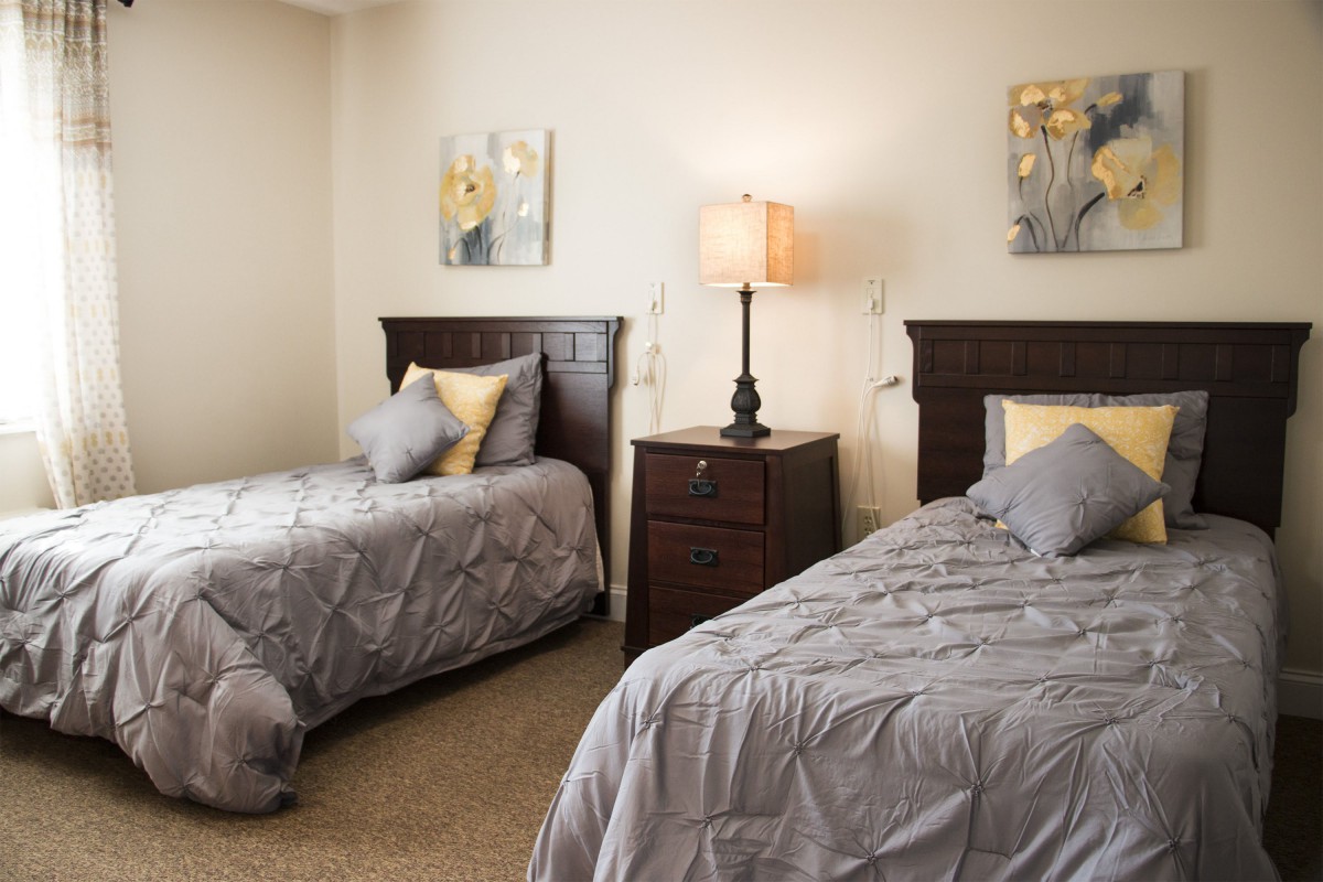 A cozy bedroom with two twin beds and a shared nightstand with a lamp.