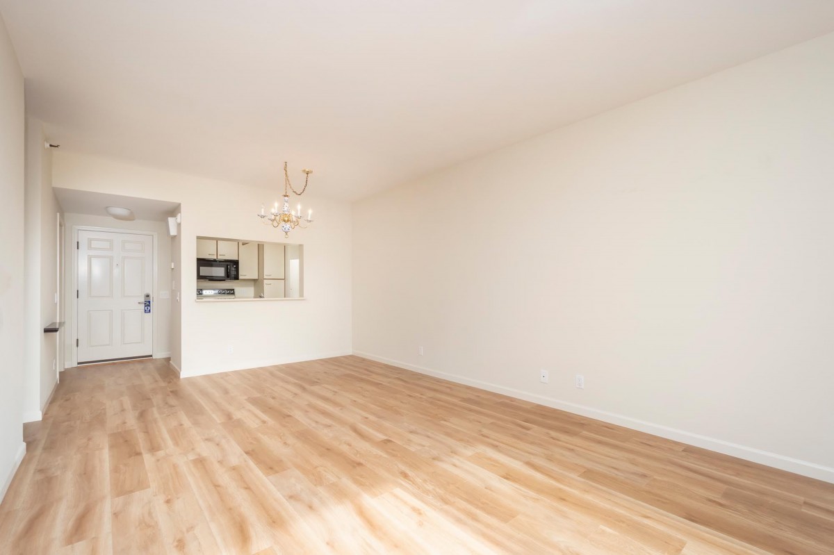 A spacious and minimalist empty room with wooden floors and white walls, featuring a chandelier.