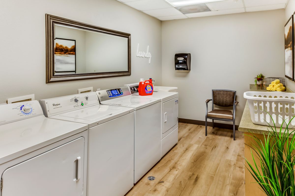 A tidy laundry room with a washing machine, dryer, and a chair on hardwood flooring.