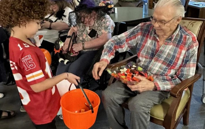 A child in costume receives candy from an elderly person during a Halloween event.