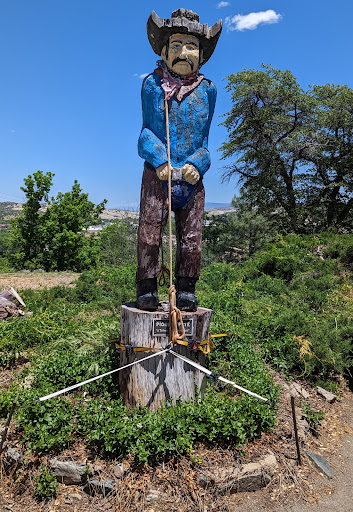 A large statue of a man standing on a tree stump, surrounded by greenery.