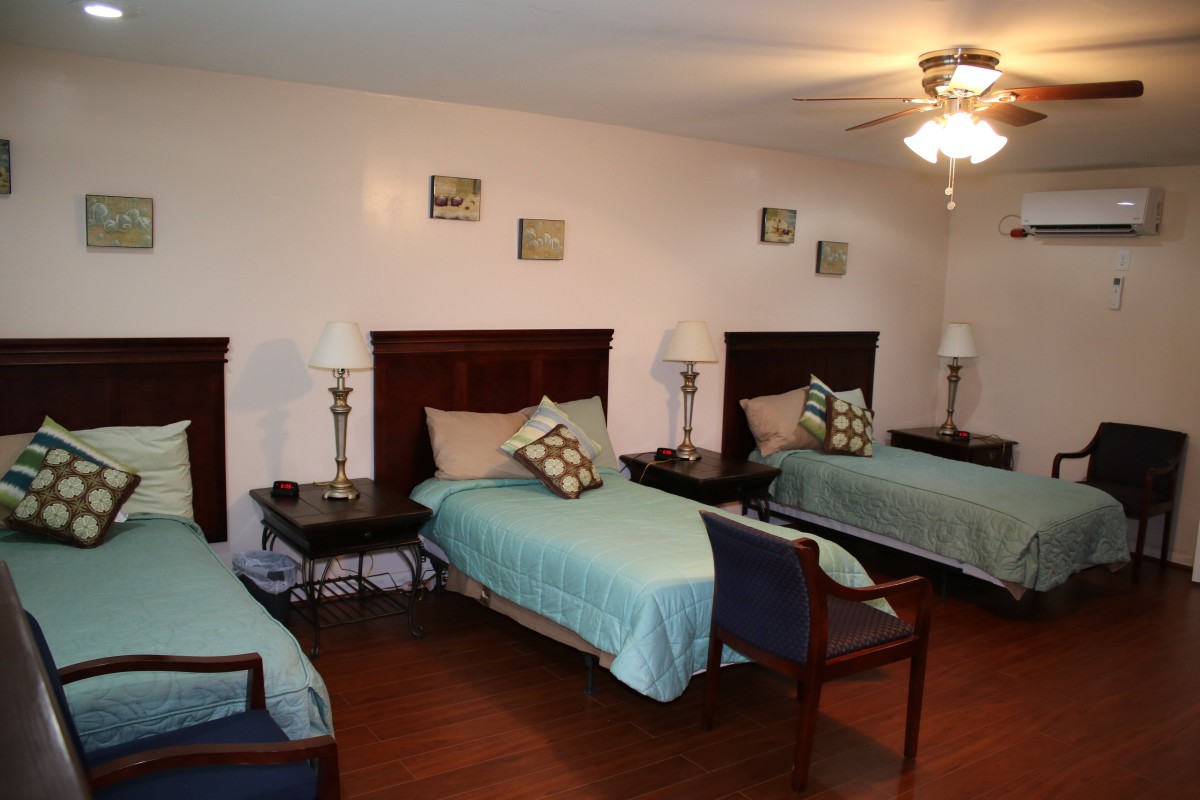 A cozy bedroom featuring three single beds with matching bedding, complemented by lamps and a ceiling fan.