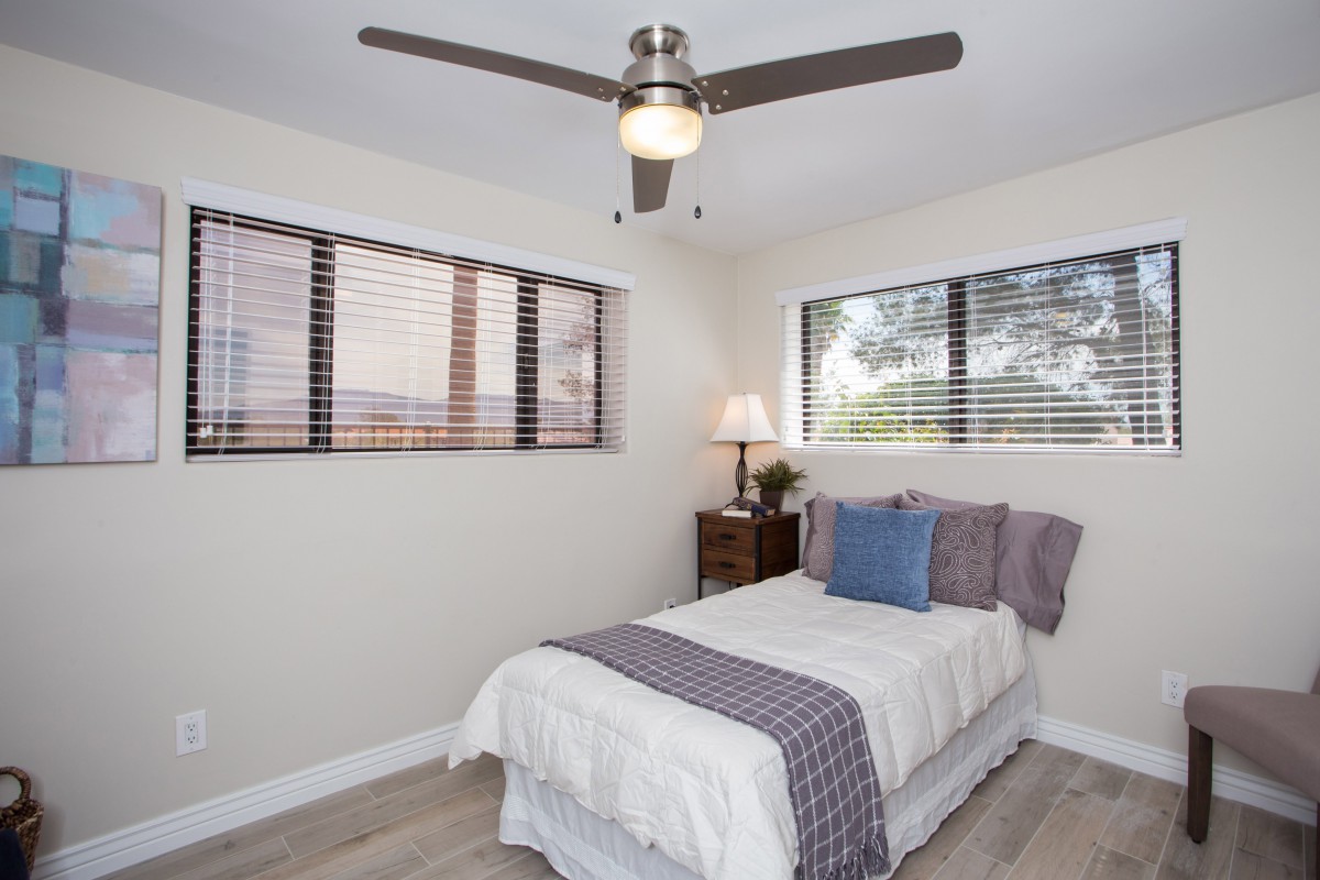 A simple and minimalist bedroom with a bed, ceiling fan, and natural light from the windows.