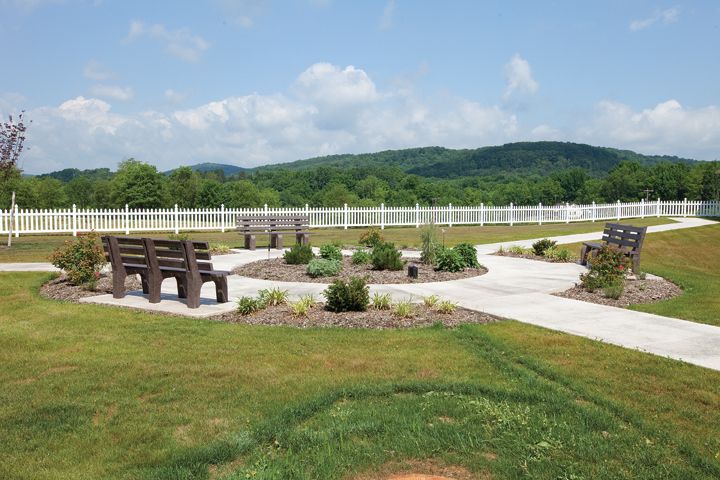 A scenic outdoor park with benches, walking paths, and lush greenery against a backdrop of hills.