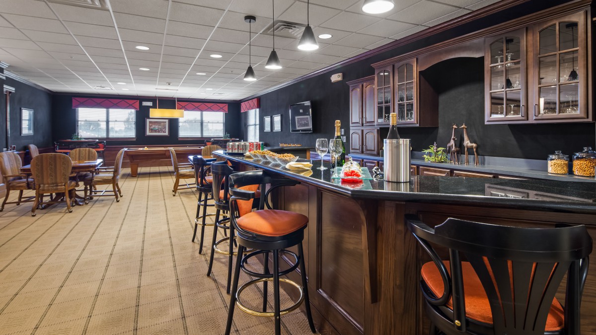 A modern bar interior with a sleek counter and comfortable stools, accented by stylish lighting.