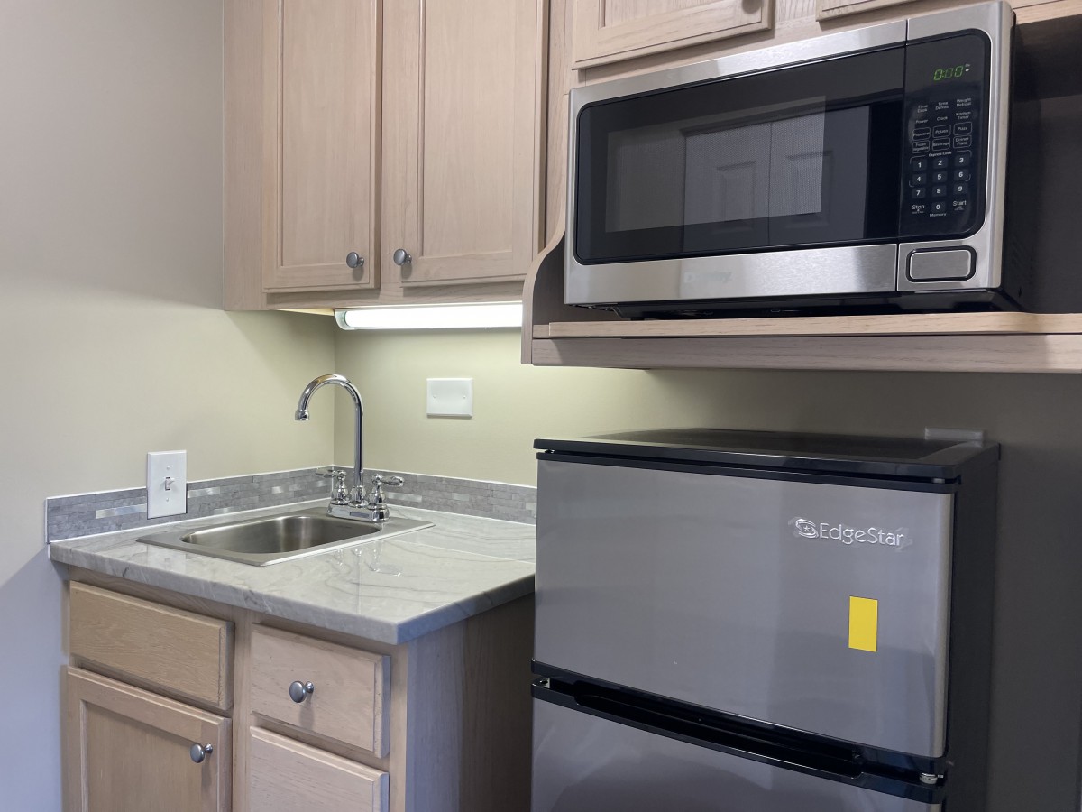 A compact kitchen area featuring a microwave, refrigerator, sink, and cabinets.