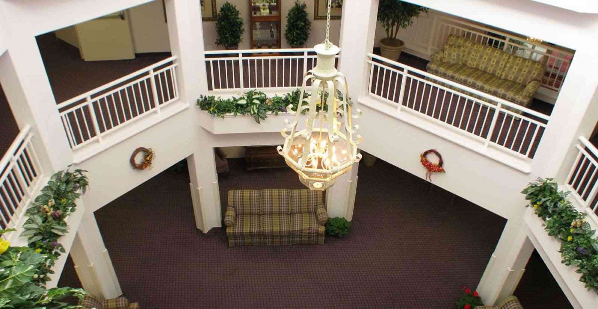 A spacious lobby with a chandelier, sofa, and decorative plants.