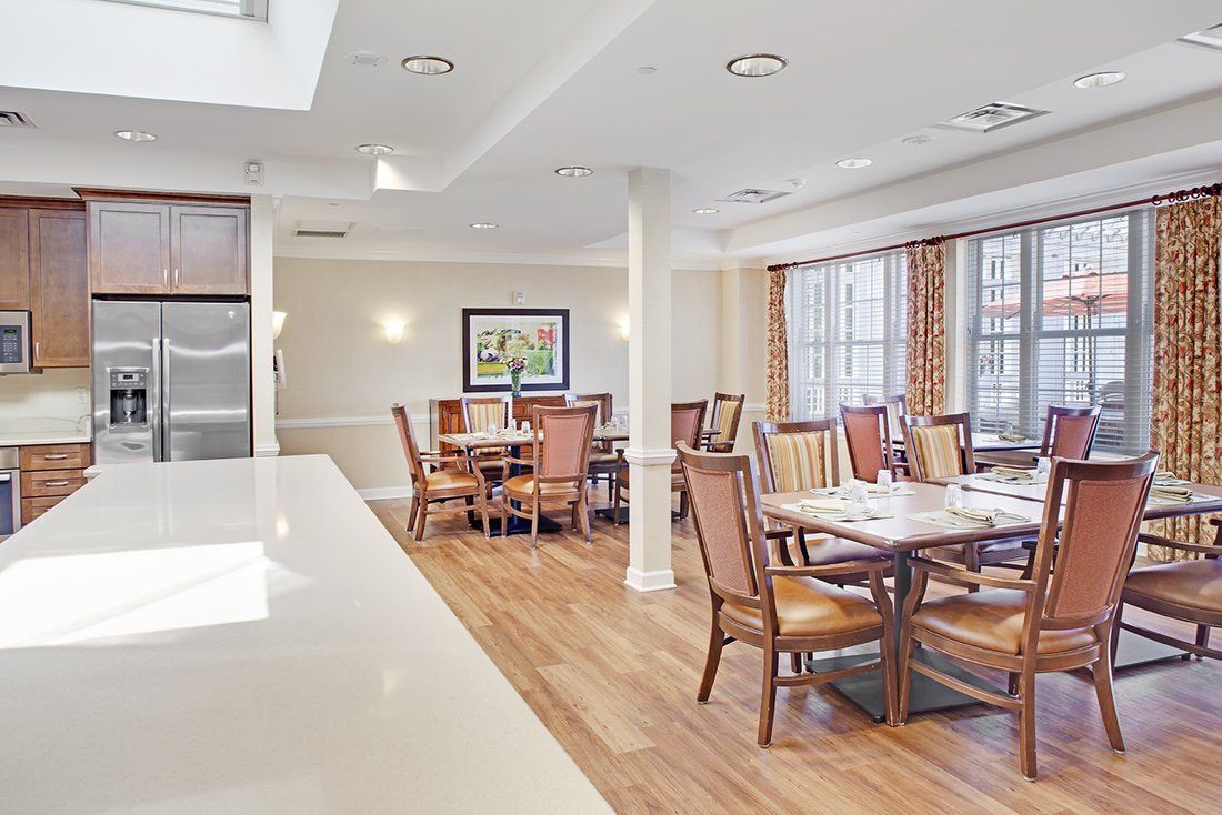 A modern dining room with neatly arranged tables and chairs, featuring large windows and bright lighting.