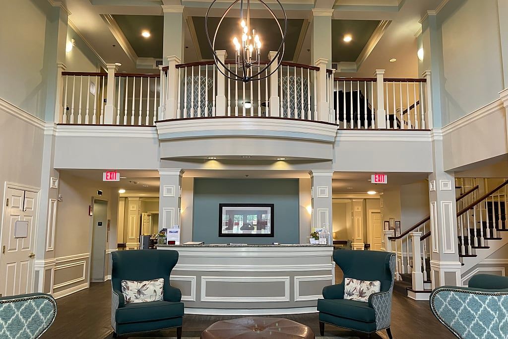 A spacious and elegant hotel lobby featuring a central chandelier, seating area, and grand staircase.