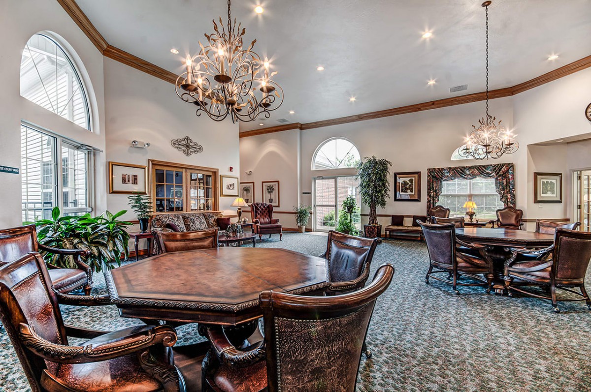 A spacious and elegant living room featuring a large wooden table and chairs, with chandeliers and tasteful decor.