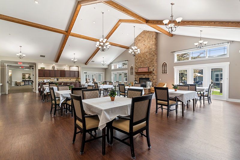 A spacious dining room with wooden ceilings, chandeliers, and a fireplace, featuring tables set for meals.
