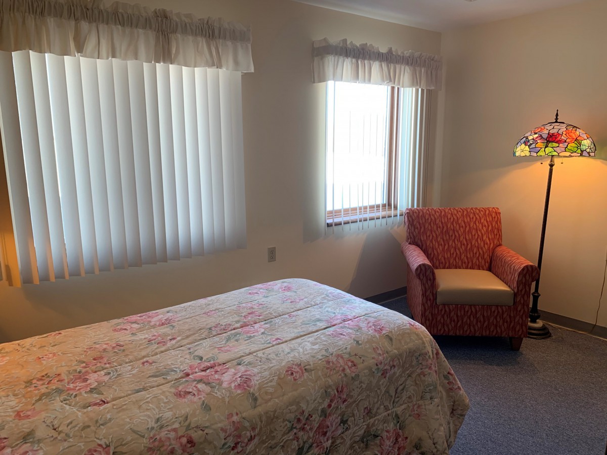 A cozy bedroom with a floral-patterned bedspread, featuring a cushioned armchair by the window.