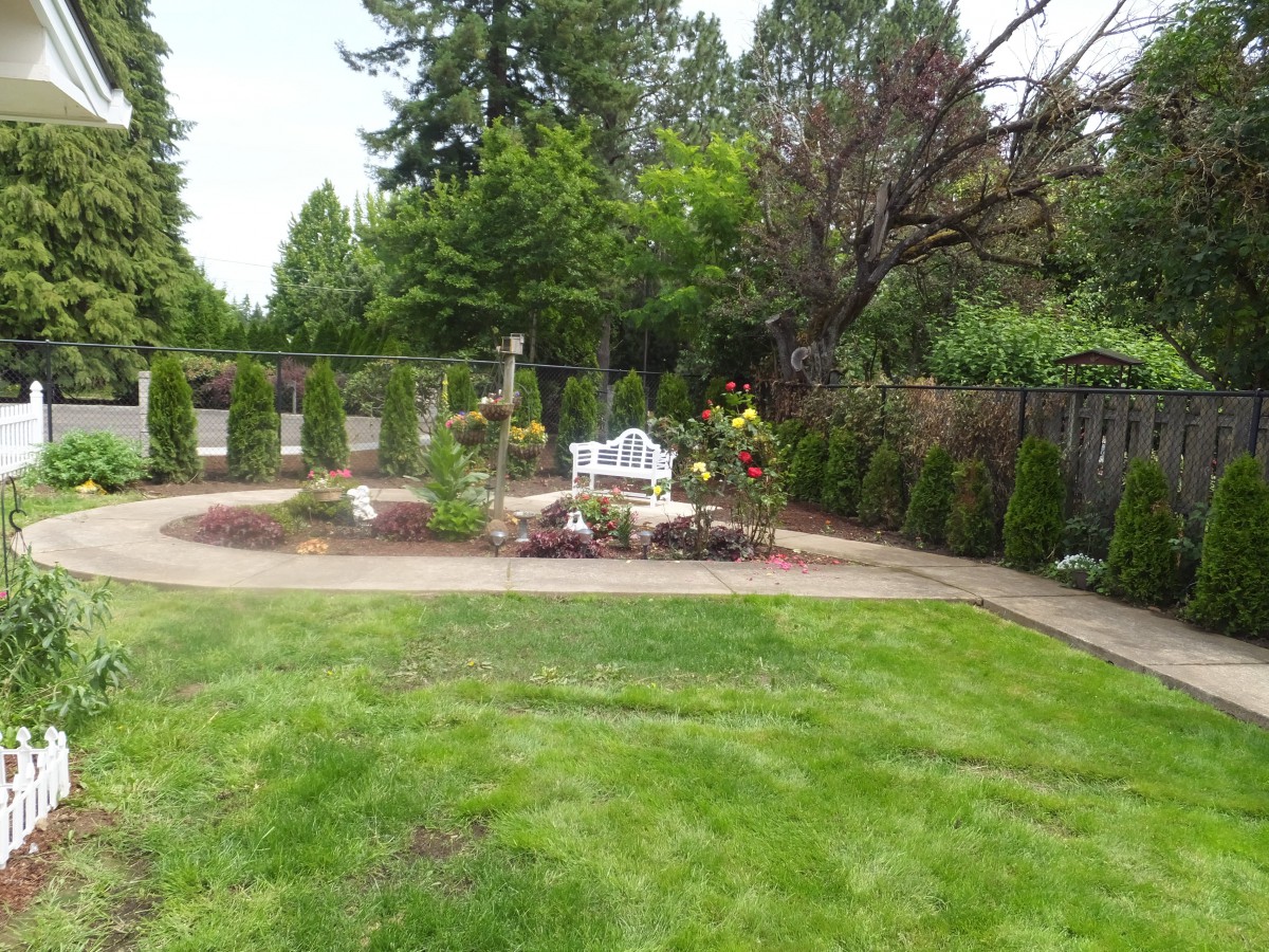 A well-maintained garden with a bench, surrounded by trees and a grassy lawn.