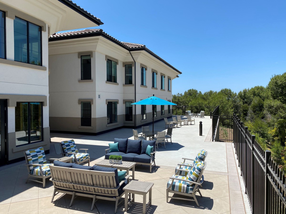 A sunny outdoor patio with comfortable seating and umbrellas beside a building.