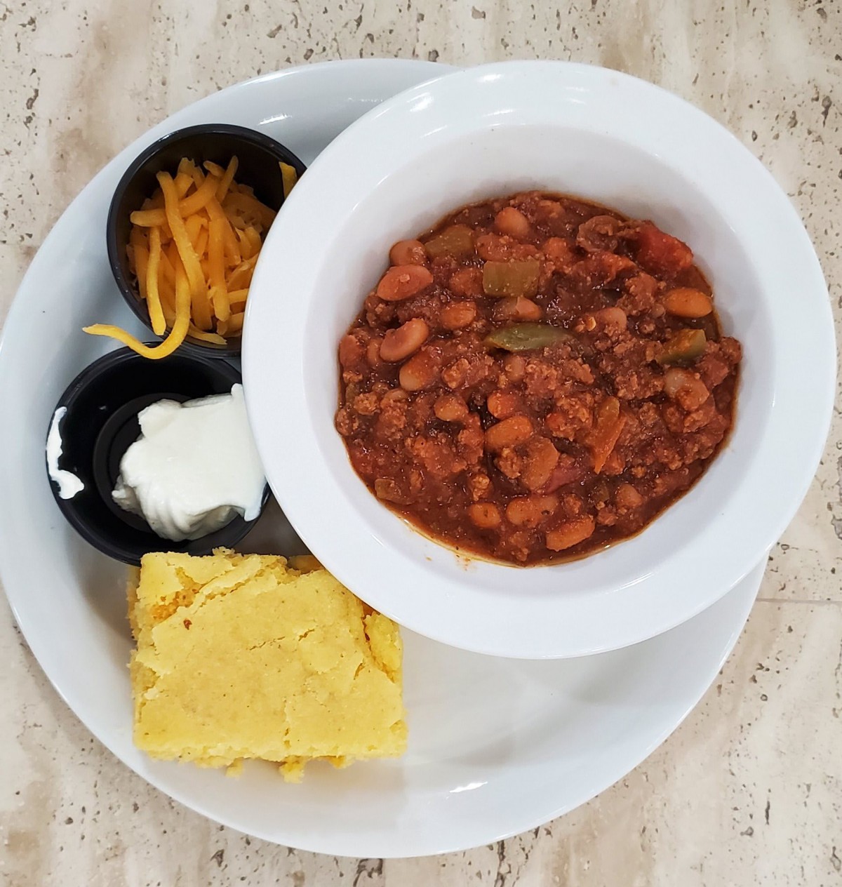 A hearty meal featuring a bowl of chili accompanied by cornbread, shredded cheese, and sour cream.