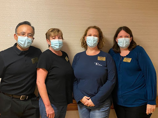 A group of staff members posing for a photo indoors while wearing masks.