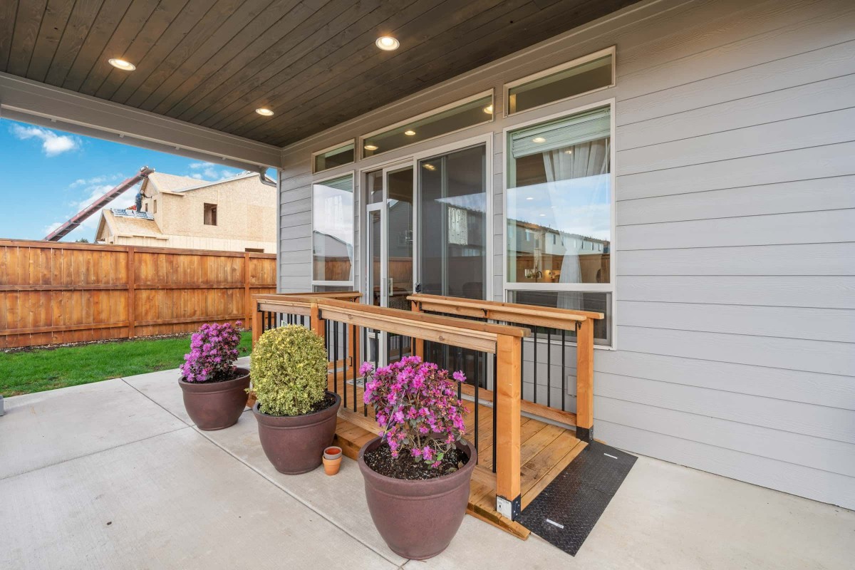 A cozy porch with potted plants and a wooden railing overlooking a backyard.