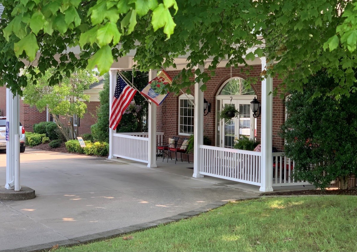 A house with a porch adorned with flags and surrounded by greenery.