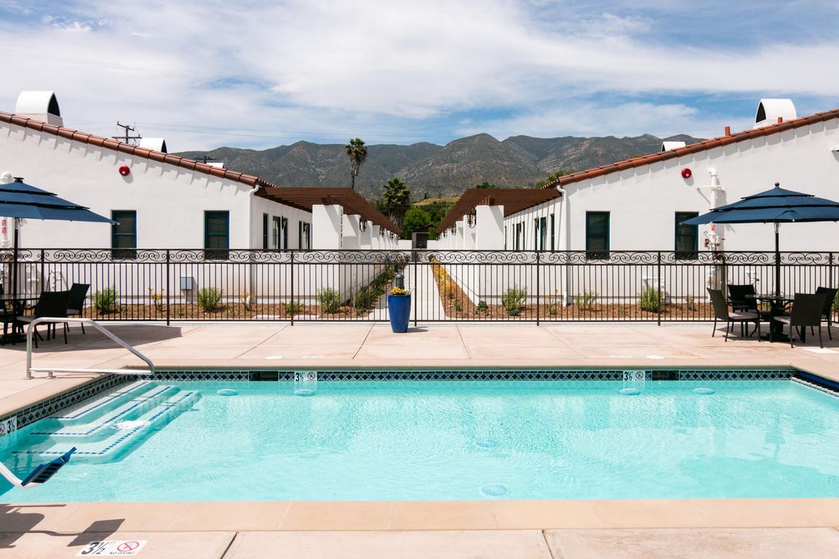 A view of a swimming pool in a residential area with white buildings and mountains in the background.