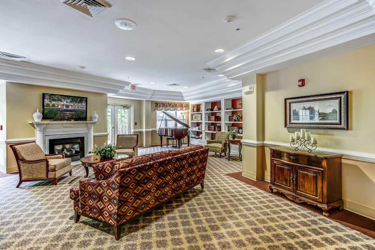 A cozy living room with a patterned couch, bookshelves, carpeted floor, and a piano.
