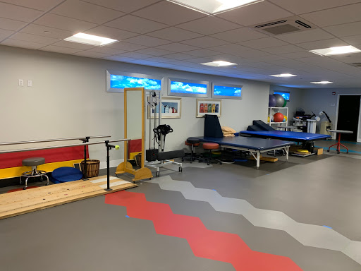 A spacious gym area designed for physical therapy and fitness training, featuring various exercise equipment and colorful flooring.
