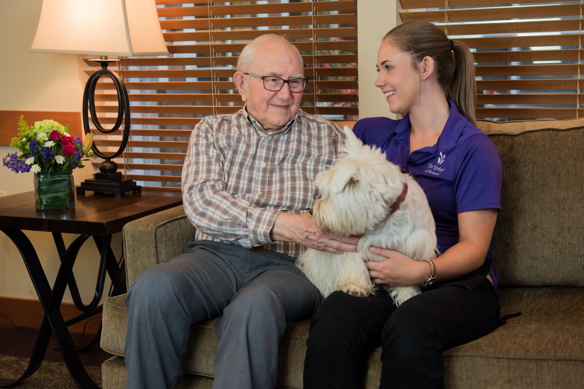 An elderly man and a young woman sitting on a couch with a dog, enjoying a moment of companionship.