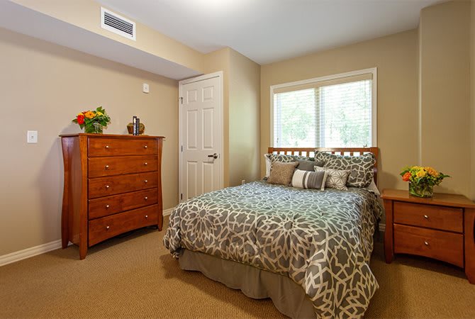 A cozy bedroom featuring a wooden dresser and a bed with patterned bedding.