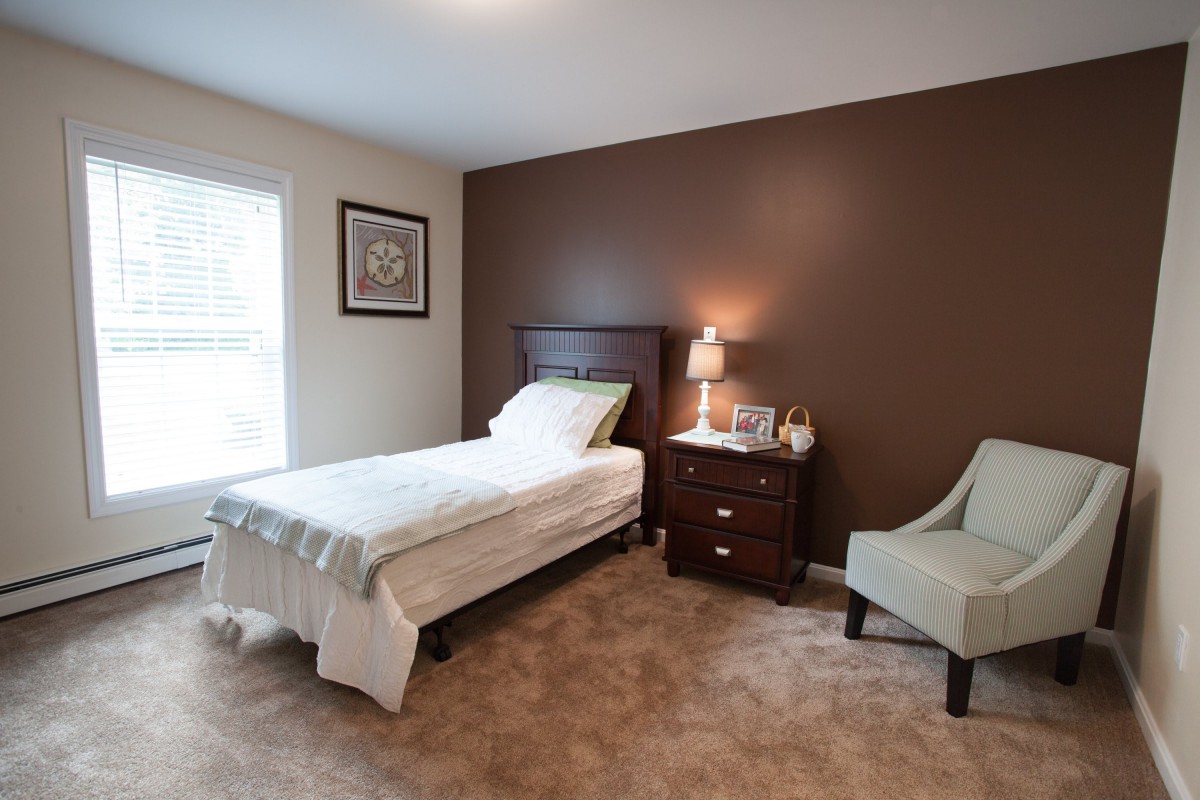 A cozy bedroom with a single bed, nightstand, and armchair.