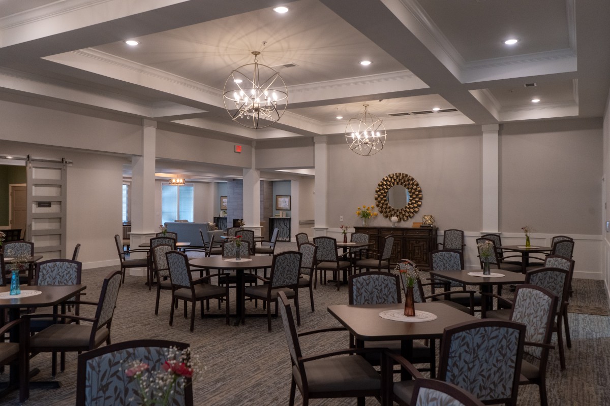 Elegant dining room with multiple tables and chairs, softly lit by chandeliers.