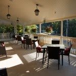 A sunlit outdoor dining area with tables and chairs, adorned with hanging plants and lanterns.