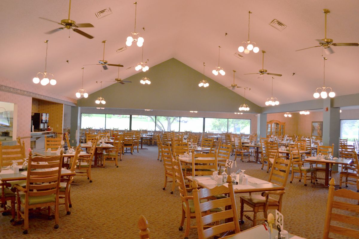 Spacious dining area with wooden tables and chairs, featuring large windows and ceiling lights.