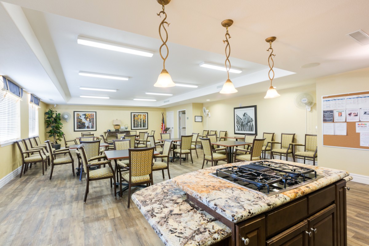 A spacious dining area with multiple tables and chairs, featuring a central kitchen island under elegant lighting fixtures.