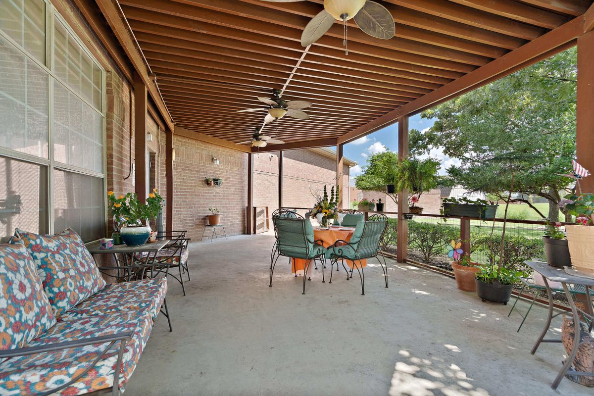 A cozy patio with comfortable seating and ceiling fans overlooking a lush garden.