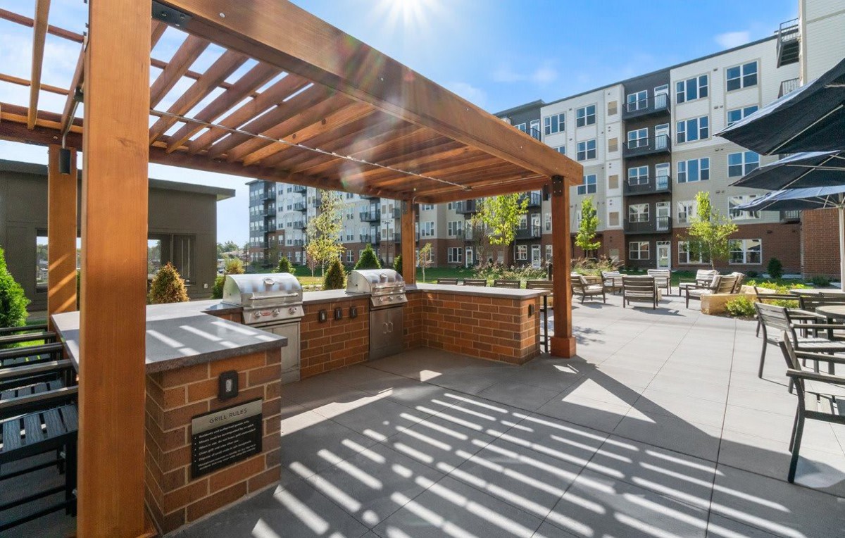 A modern outdoor patio area with a pergola and barbecue grills at an apartment complex.