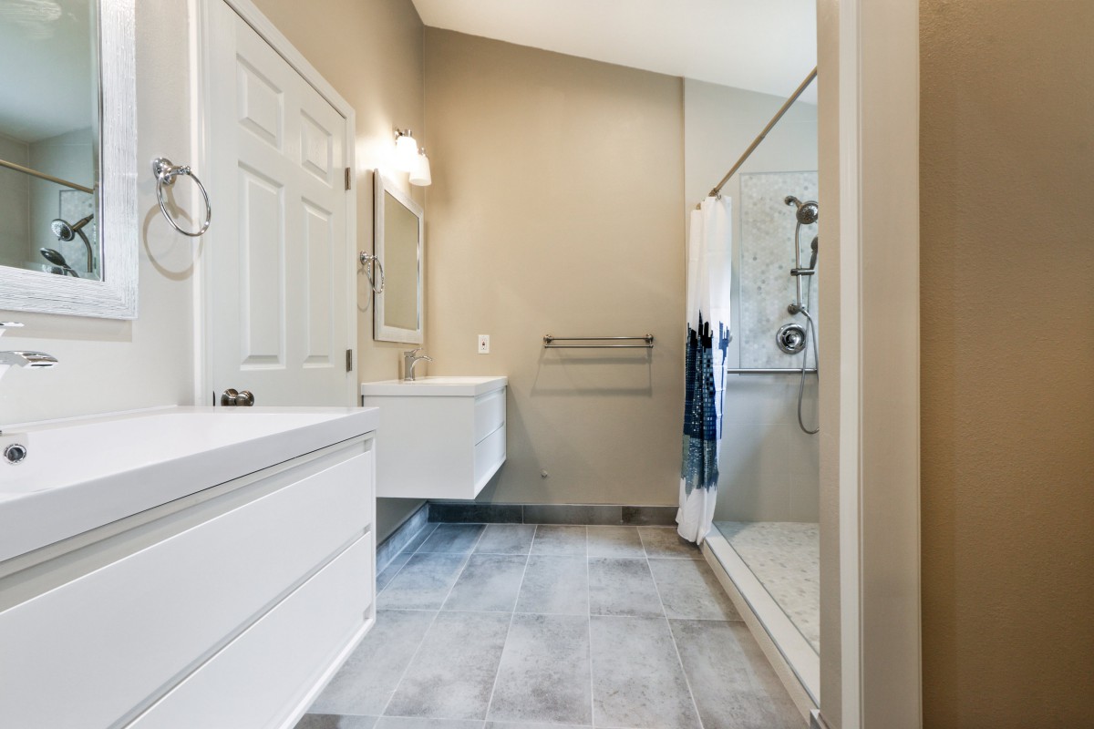 A modern bathroom with a glass shower, a mirror above the sink, and neutral-colored tiles.