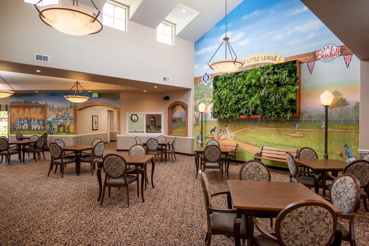 A spacious dining area with several tables and chairs, featuring a large mural and vaulted ceiling.