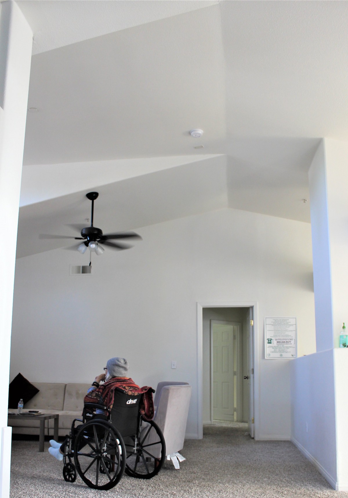 A bright, minimalist living room with a ceiling fan and doorway.