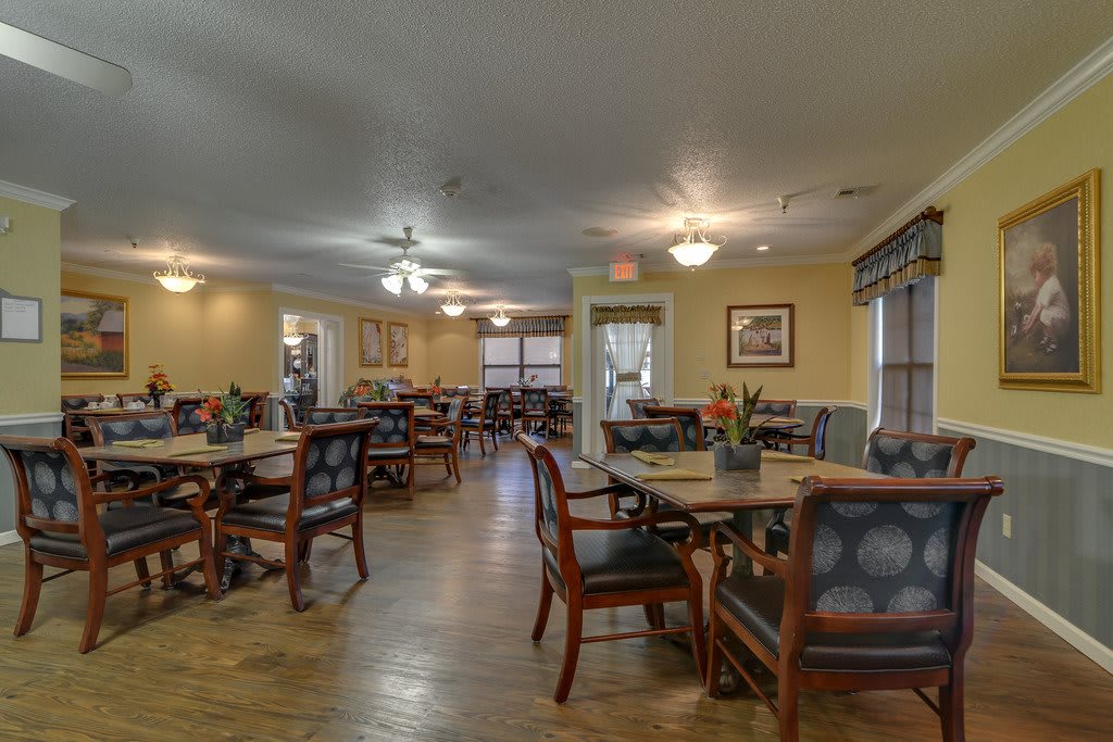 A spacious dining area with neatly arranged tables and chairs, featuring soft lighting and large windows.